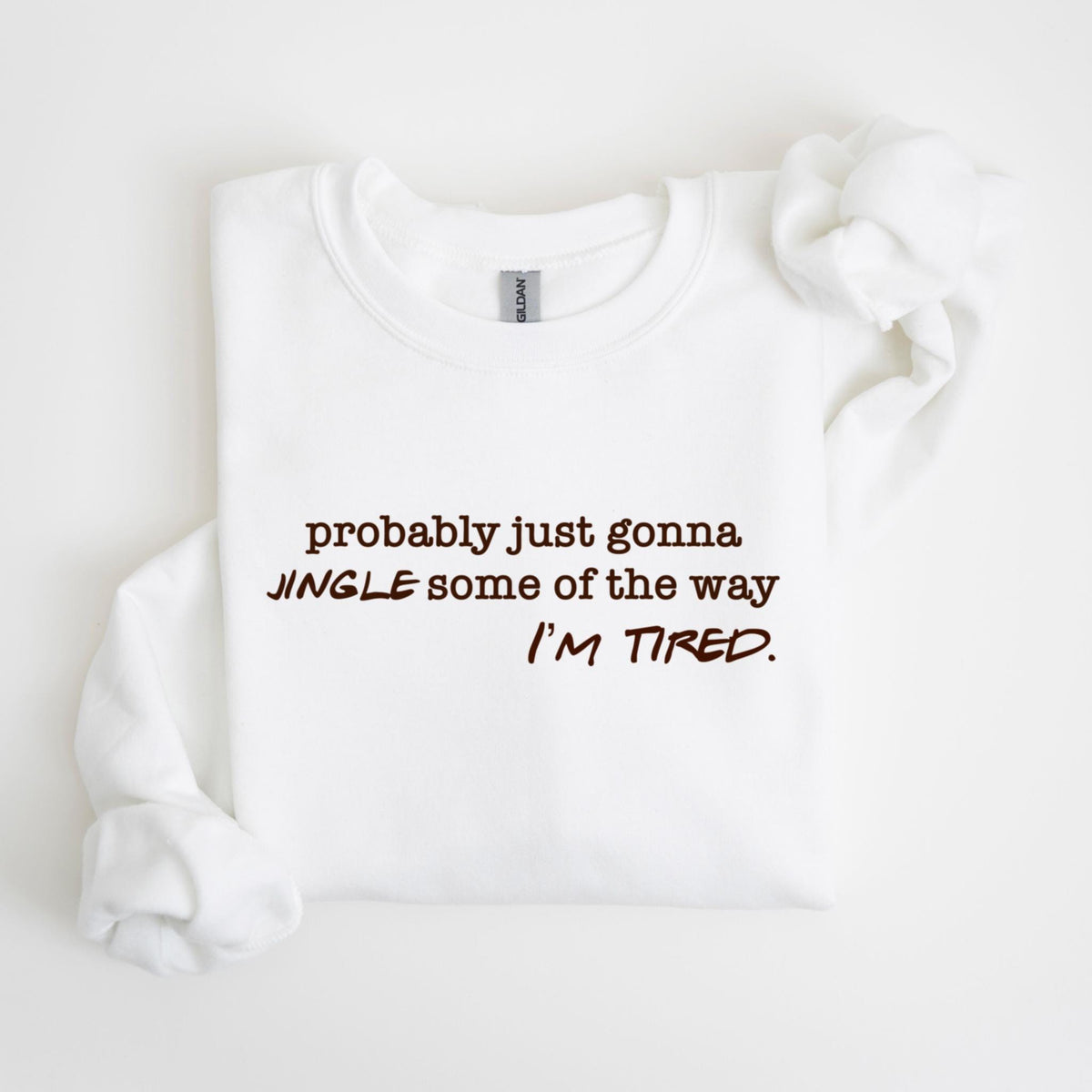May include: White crew neck sweatshirt with the text "probably just gonna jingle some of the way I'm tired" in brown lettering. The sweatshirt is folded with the sleeves and collar visible.