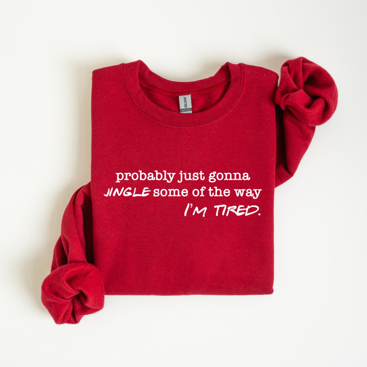 May include: A red crewneck sweatshirt with white text that reads "probably just gonna JINGLE some of the way I'M TIRED." The sleeves are folded. The sweatshirt is on a white background.