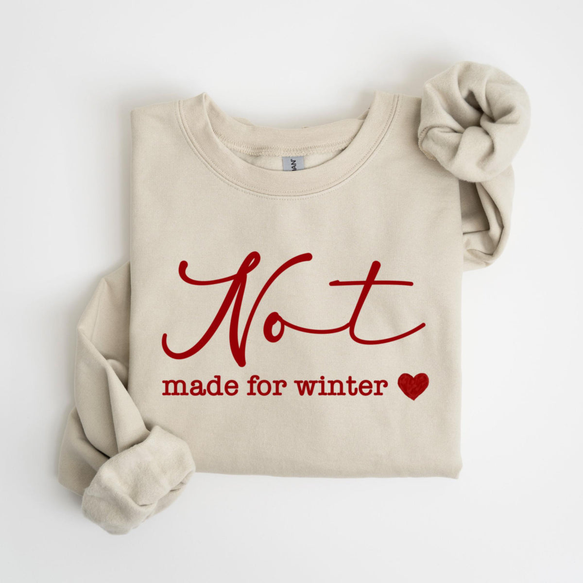 May include: A beige sweatshirt with the words "Not made for winter" in red script. A red heart is next to the text. The sleeves are folded and the sweatshirt is laying flat.