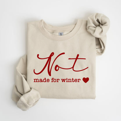 May include: A beige sweatshirt with the words "Not made for winter" in red script. A red heart is next to the text. The sleeves are folded and the sweatshirt is laying flat.