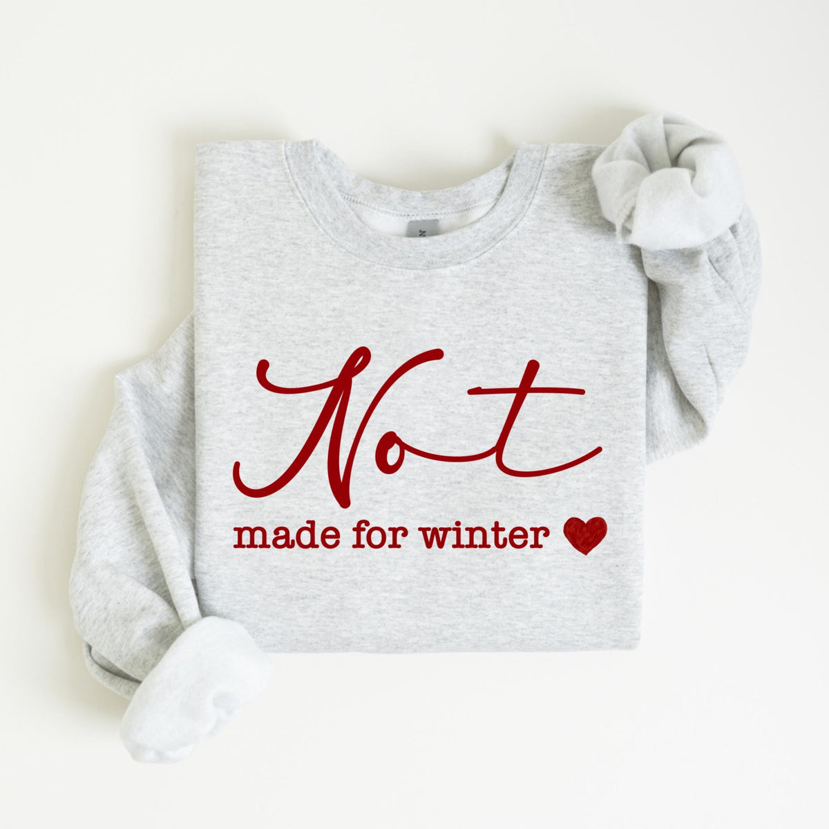 May include: A light gray sweatshirt with the words "Not made for winter" in red script and a red heart. The sweatshirt has long sleeves and a crew neck.