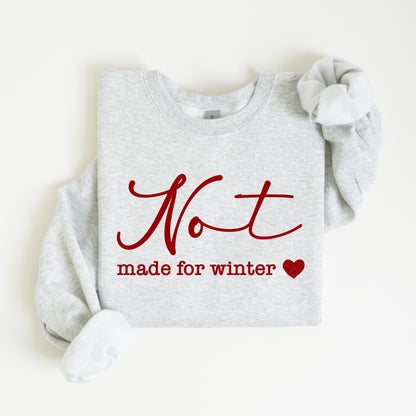 May include: A light gray sweatshirt with the words "Not made for winter" in red script and a red heart. The sweatshirt has long sleeves and a crew neck.