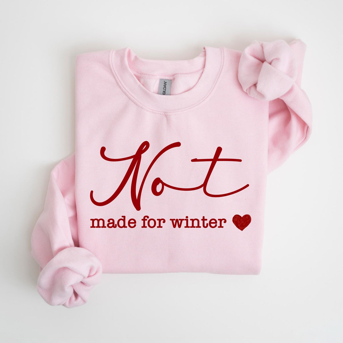 May include: A light pink sweatshirt with the words "Not made for winter" in a burgundy script. A small burgundy heart is below the text. The sweatshirt has long sleeves and a crew neck.