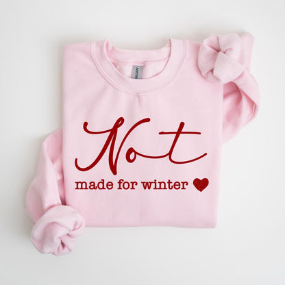 May include: A light pink sweatshirt with the words "Not made for winter" in a burgundy script. A small burgundy heart is below the text. The sweatshirt has long sleeves and a crew neck.