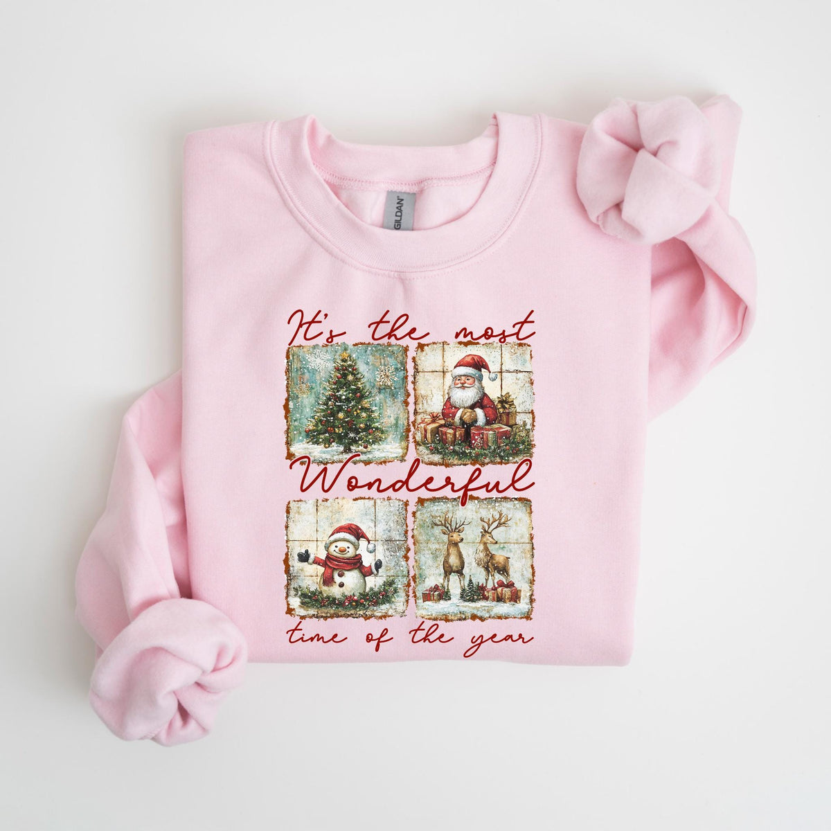 May include: A light pink sweatshirt featuring a Christmas-themed graphic. The graphic includes a Christmas tree, Santa Claus, a snowman, and reindeer, with the text "It's the most Wonderful time of the year."