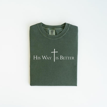 May include: A dark green t-shirt with the text "His Way Is Better" in white, along with a white cross. The shirt is folded neatly and is displayed on a white background. The shirt is made of a soft material.