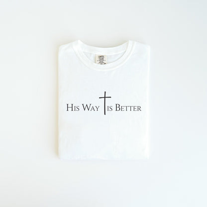 May include: A folded white t-shirt with the text "His Way Is Better" in black, with a cross symbol. The shirt is made of a soft material and is neatly folded, ready to wear.