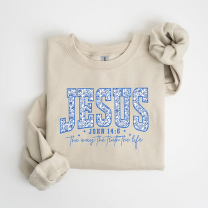 May include: A beige sweatshirt with the word "JESUS" in blue floral lettering. Below the word "JESUS" is the text "JOHN 14:6" and "The way the truth the life" in blue script. The sweatshirt has long sleeves.