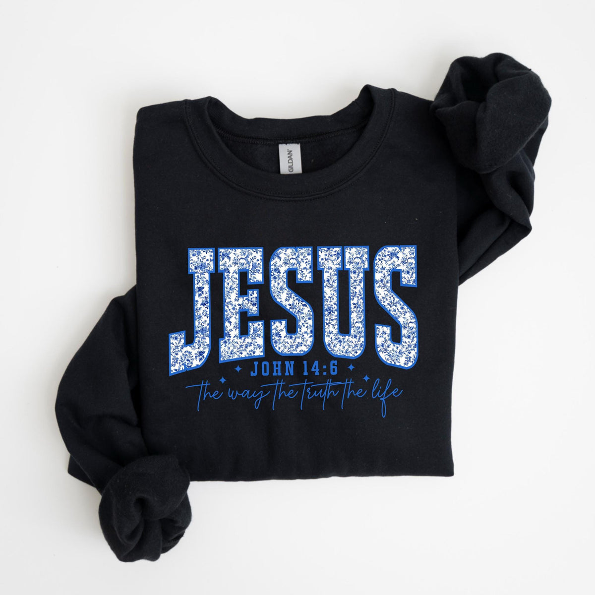 May include: Black long-sleeve sweatshirt with the word "JESUS" in large, blue floral letters. Below, the text reads "JOHN 14:6" and "The way the truth the life" in a matching blue font. The sweatshirt is folded.