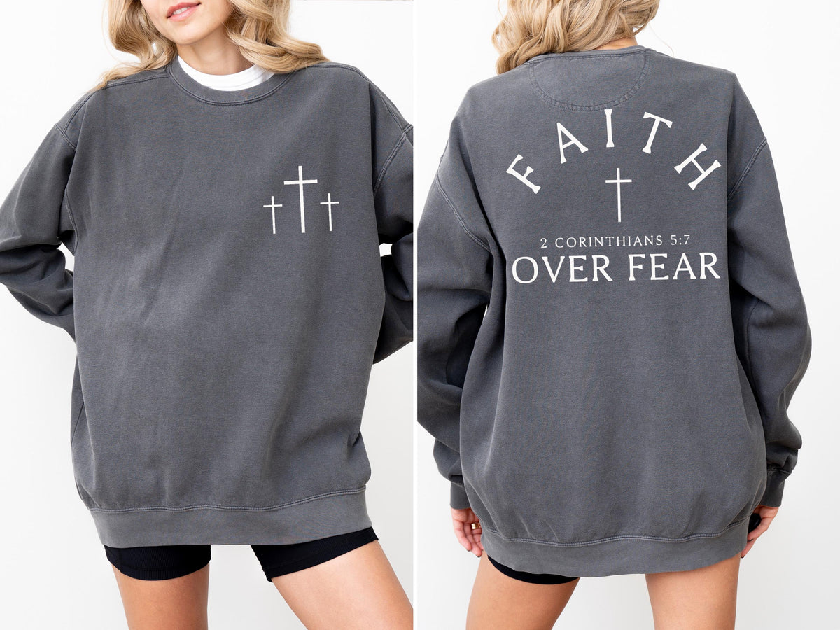 May include: Charcoal gray sweatshirt with three white crosses on the front. The back of the sweatshirt features the word "FAITH" above a cross, with "2 CORINTHIANS 5:7 OVER FEAR" printed below. A casual, comfortable style.