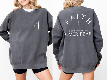 May include: Charcoal gray sweatshirt with three white crosses on the front. The back of the sweatshirt features the word "FAITH" above a cross, with "2 CORINTHIANS 5:7 OVER FEAR" printed below. A casual, comfortable style.