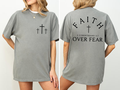 May include: A gray t-shirt with three black crosses on the front and the text "FAITH OVER FEAR" with a cross and the Bible verse 2 Corinthians 5:7 on the back. The shirt is a casual, oversized style.