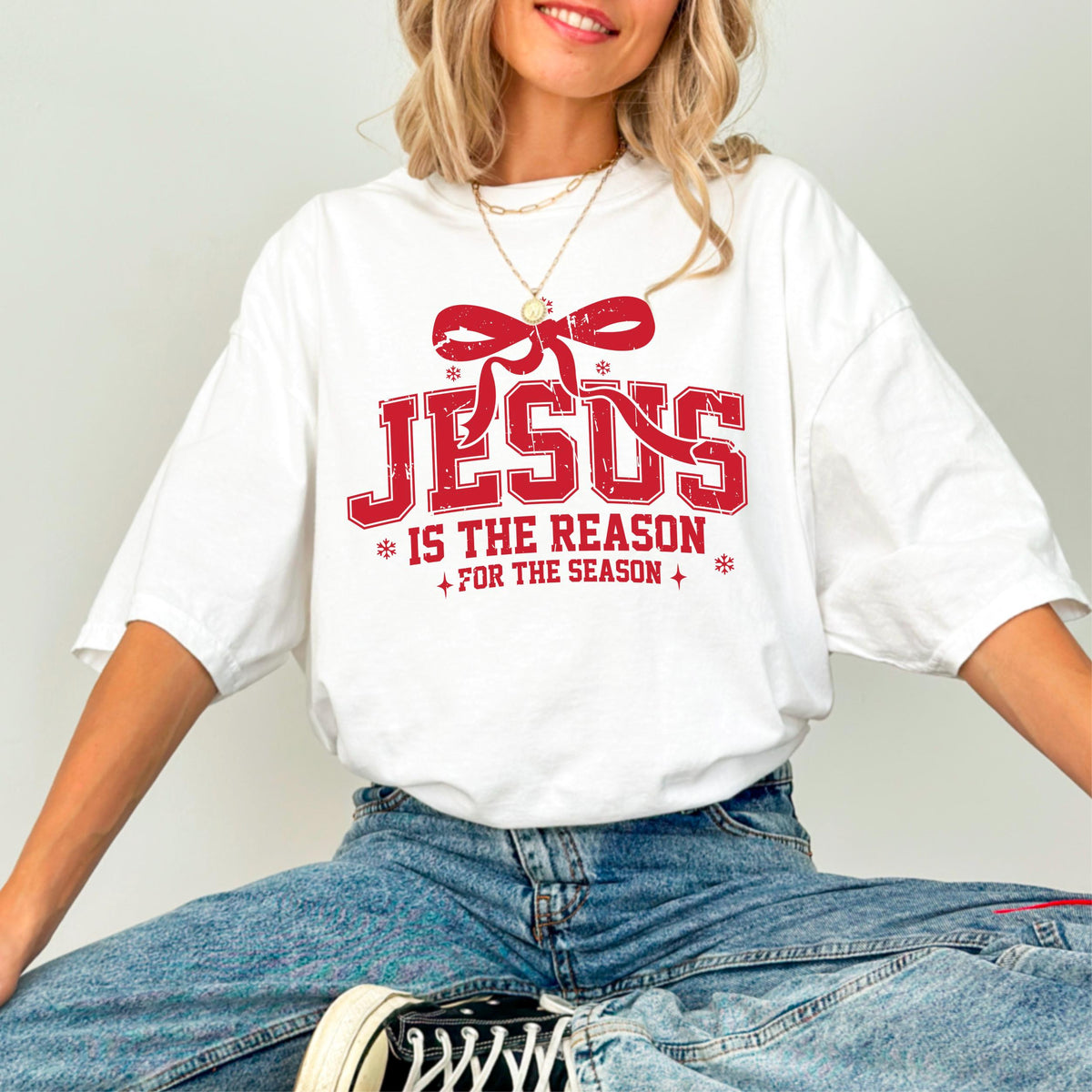 May include: White t-shirt with a red graphic that reads "JESUS IS THE REASON FOR THE SEASON." The design includes a red bow and snowflakes. The shirt is a casual, oversized fit.