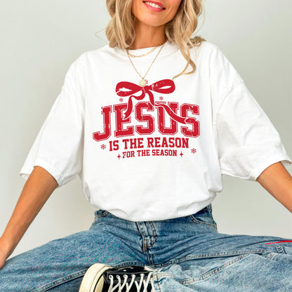 May include: White t-shirt with a red graphic that reads "JESUS IS THE REASON FOR THE SEASON." The design includes a red bow and snowflakes. The shirt is a casual, oversized fit.