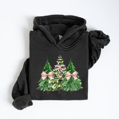 May include: A black hooded sweatshirt featuring a watercolor design of three Christmas trees. The trees are green with pink bows, and the middle tree has a pink bow and garland. The sweatshirt is folded on a white surface.