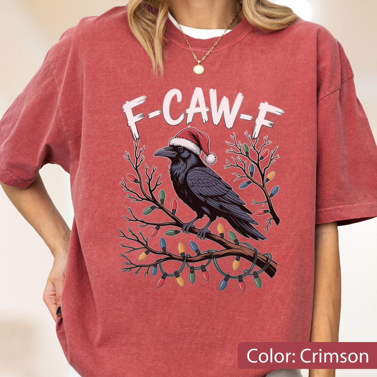 May include: A crimson short-sleeve t-shirt featuring a graphic of a black crow wearing a red and white Santa hat, perched on a branch wrapped in colorful Christmas lights. The text F-CAW-F is printed in white above the crow illustration.