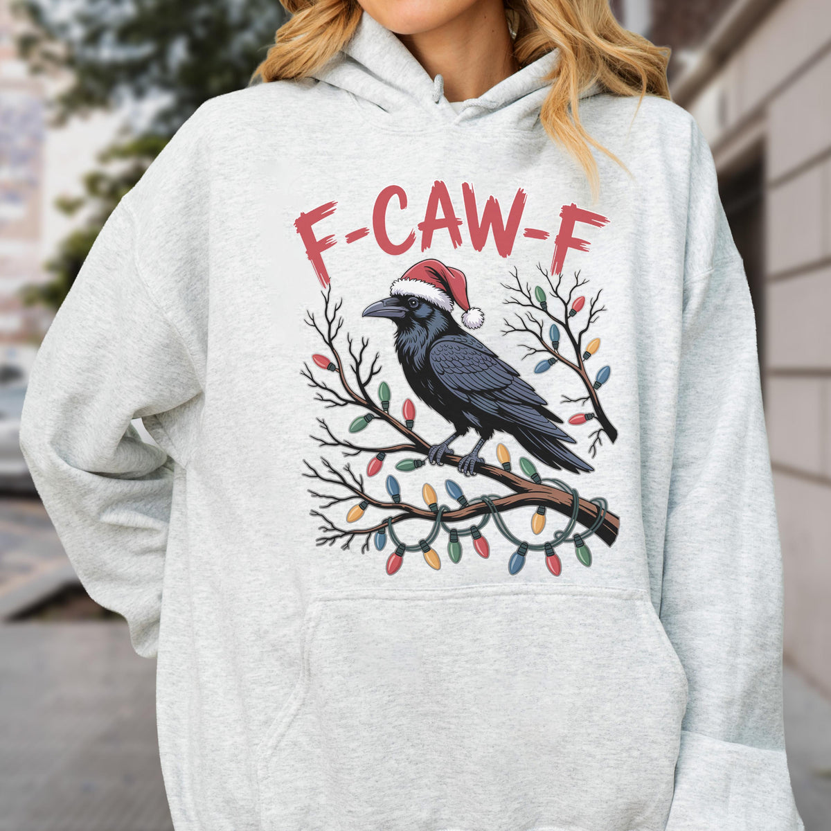 May include: A light gray heathered hoodie featuring a graphic of a black crow wearing a red and white Santa hat, perched on a tree branch wrapped in colorful Christmas lights, with the red text F-CAW-F printed above the bird illustration.