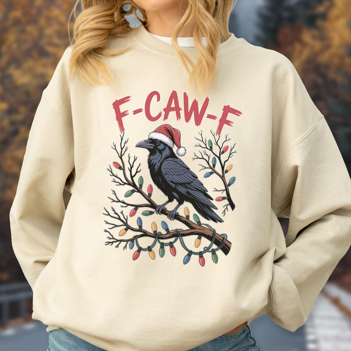 May include: A beige crewneck sweatshirt featuring a graphic of a black raven wearing a red and white Santa hat, perched on a bare tree branch wrapped in colorful Christmas lights, with the red text F-CAW-F printed above the bird illustration.