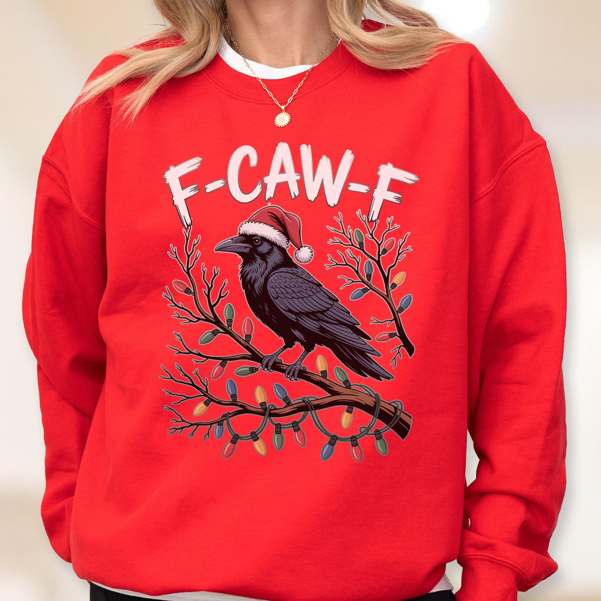 May include: A bright red crewneck sweatshirt featuring a graphic of a black crow wearing a red and white Santa hat, perched on a bare tree branch wrapped in colorful Christmas lights, with the white text F-CAW-F printed above the bird.