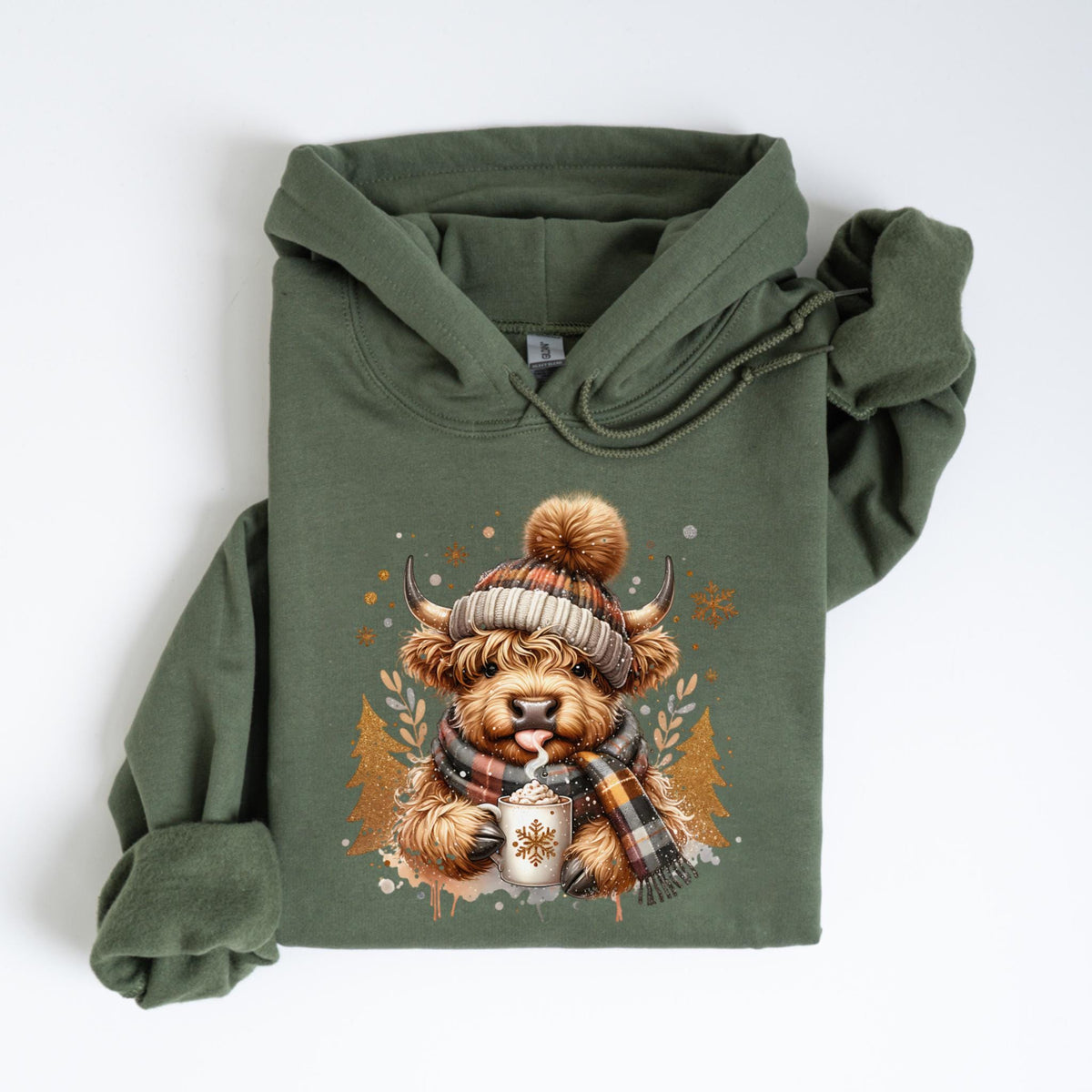 May include: An olive green hoodie featuring a graphic of a Highland cow wearing a plaid hat and scarf, holding a mug of hot cocoa. The cow has a fluffy brown coat and is sticking out its tongue. Gold and white accents complete the winter theme.