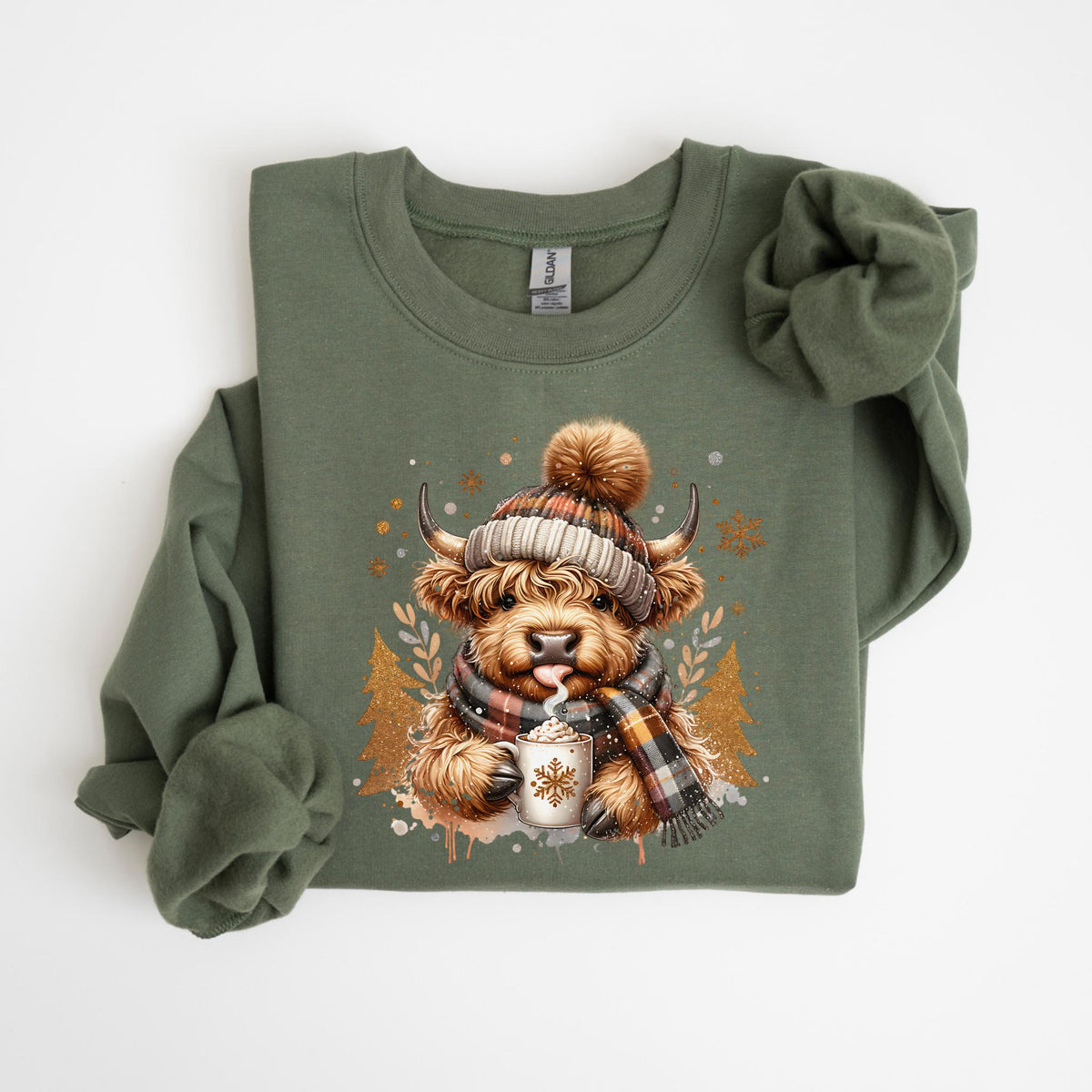 May include: Olive green sweatshirt featuring a Highland cow illustration. The cow is wearing a plaid hat and scarf, holding a mug with a snowflake design. The graphic includes gold Christmas trees and snowflakes, creating a festive winter theme.