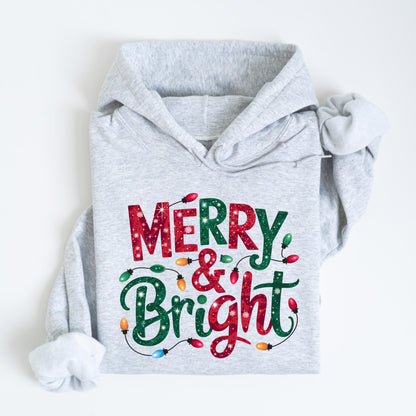 May include: A light gray hoodie with the words "MERRY & BRIGHT" in red and green, decorated with colorful Christmas lights. The hoodie is folded on a white surface.