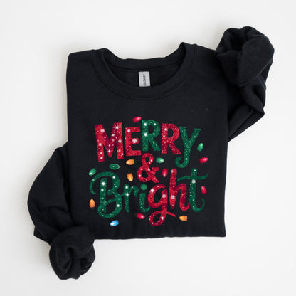May include: Black sweatshirt with the words "MERRY & BRIGHT" in red and green glitter lettering. The design includes colorful Christmas lights. The sweatshirt is folded neatly on a white surface.