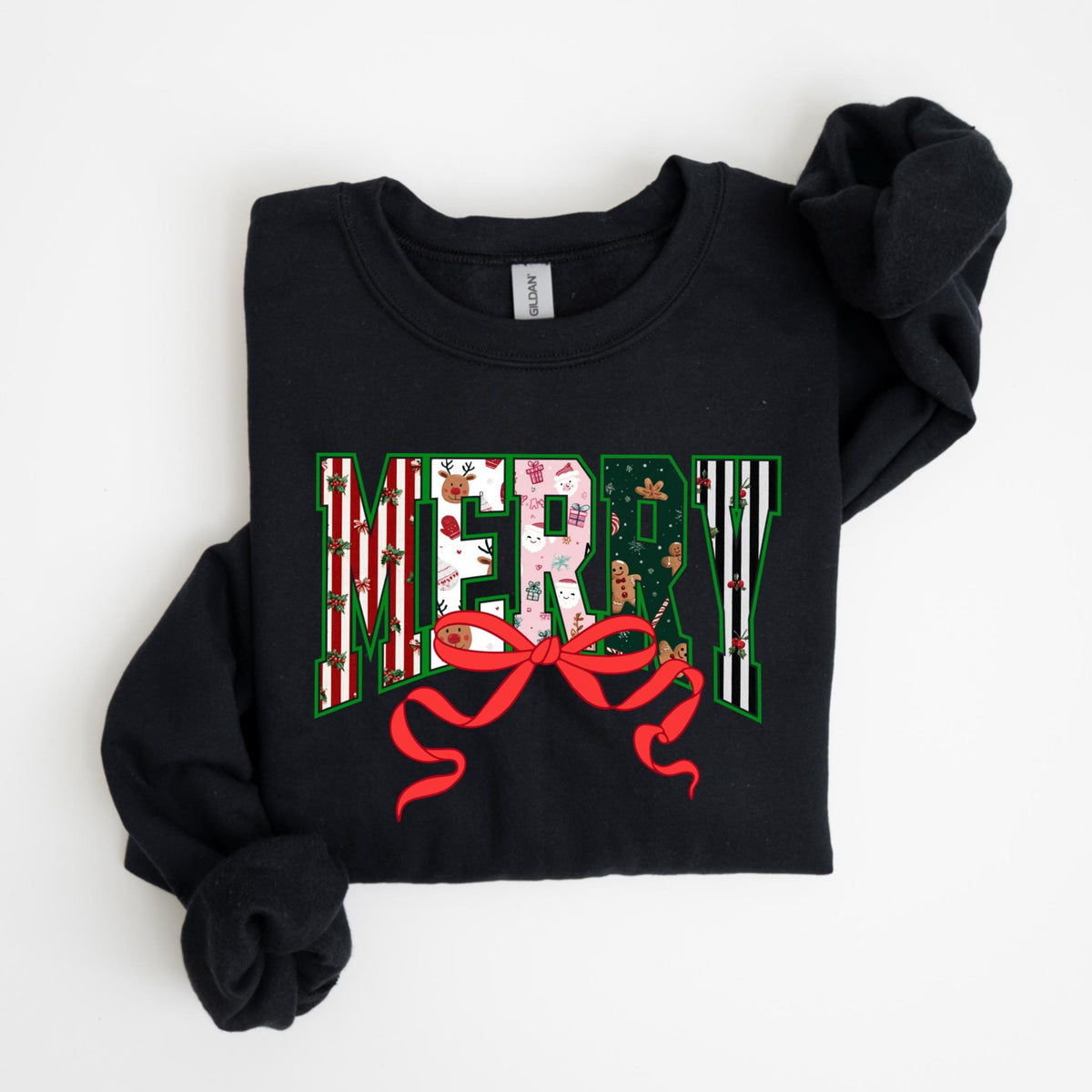 May include: Black sweatshirt with the word "MERRY" in a festive design. The letters are filled with patterns of reindeer, gifts, and gingerbread men. A red bow is at the bottom of the word. The sweatshirt is folded on a white surface.