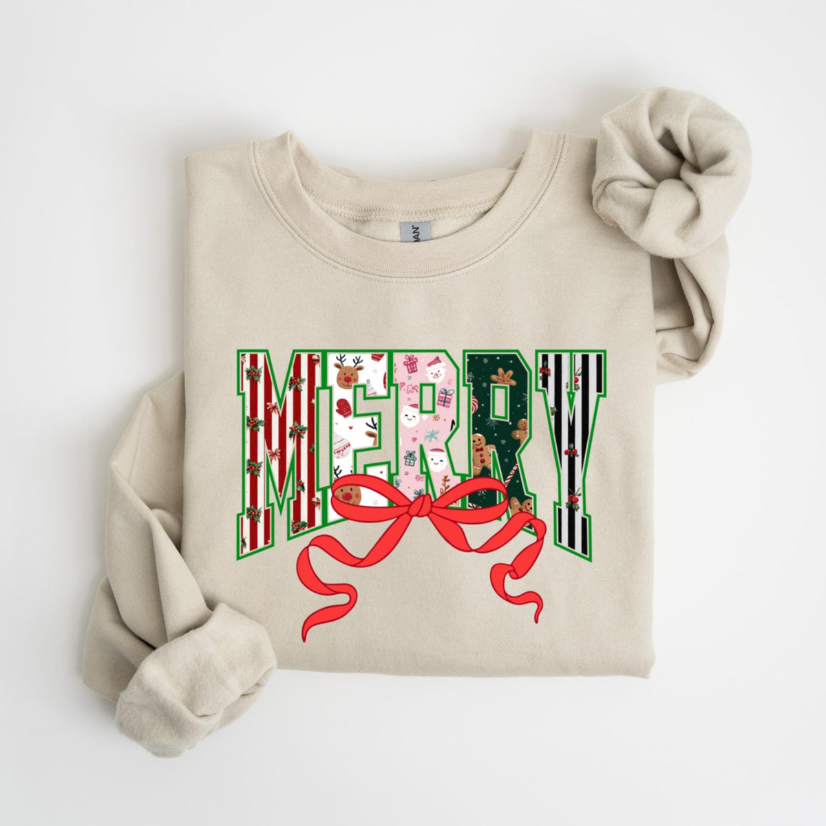 May include: Beige sweatshirt with the word "MERRY" in a festive design. The letters are filled with Christmas-themed patterns, including reindeer, gifts, and gingerbread men. A large red bow is at the bottom of the word.