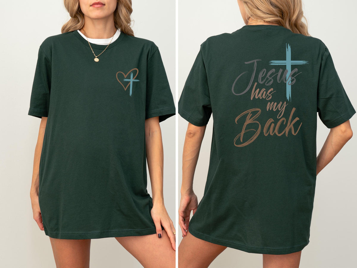 May include: Dark green t-shirt with a white collar and a gold necklace. The front of the shirt features a heart and cross design. The back of the shirt has the text "Jesus has my Back" with a cross graphic.