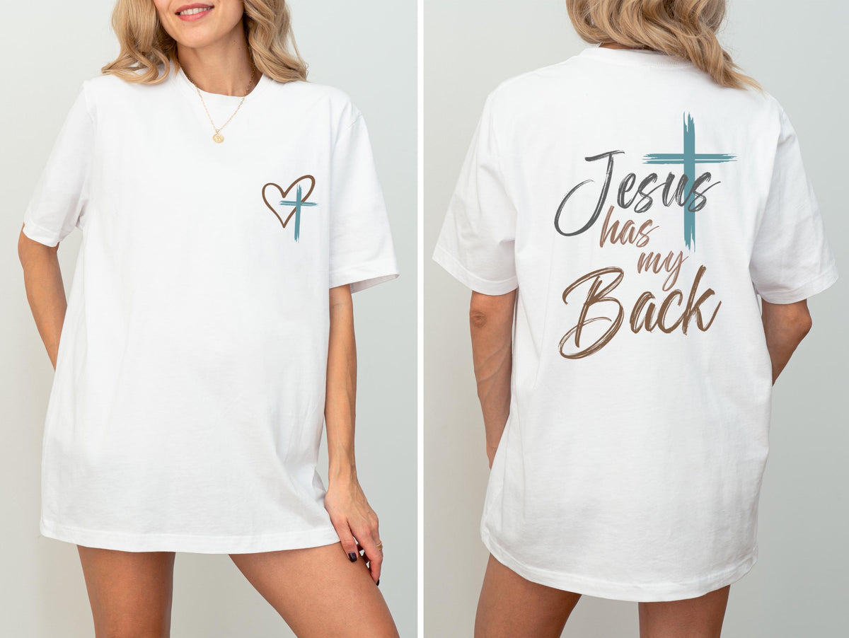 May include: White t-shirt with a heart and cross design on the front and the text "Jesus has my Back" on the back. The design features a teal cross and brown heart and text. The shirt is a short-sleeved, casual style.
