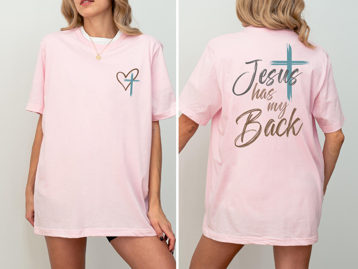 May include: A light pink t-shirt with a heart and cross design on the front. The back of the shirt features the text "Jesus has my Back" with a cross graphic. The shirt is a comfortable, casual style.