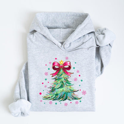 May include: A light gray hoodie featuring a colorful Christmas tree design. The tree is decorated with a pink bow, gold star, and pink and teal accents. The hoodie is folded on a white surface.
