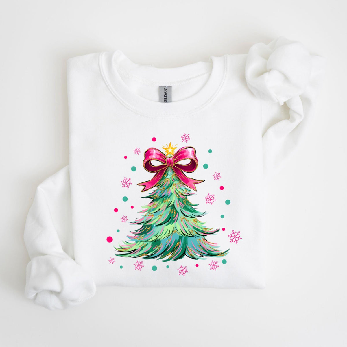 May include: White sweatshirt featuring a colorful Christmas tree design. The tree is decorated with a pink bow and a gold star. Pink snowflakes and teal dots surround the tree, creating a festive holiday theme.