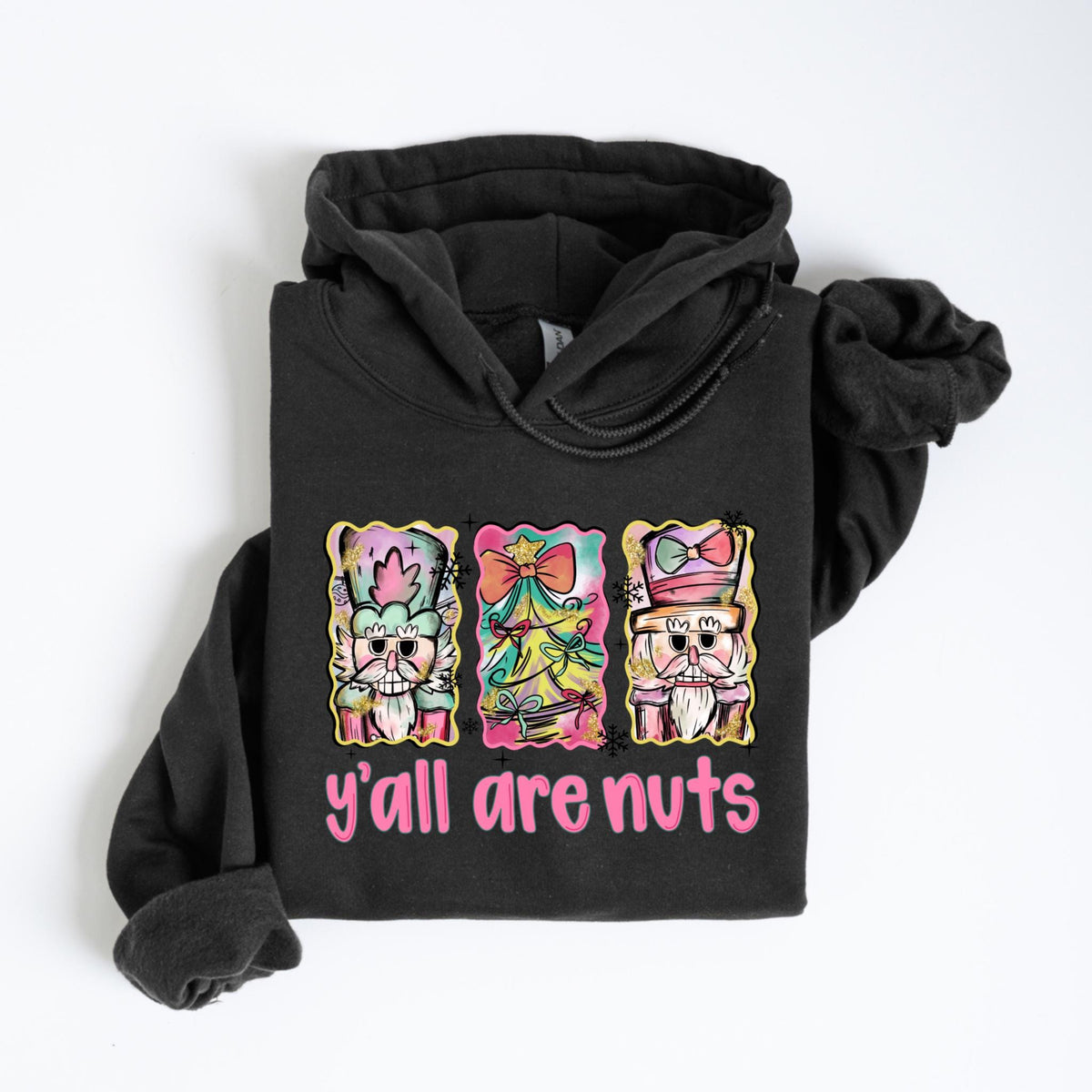 May include: A dark gray hoodie featuring a colorful graphic of three nutcrackers with the text "y'all are nuts" in pink. The nutcrackers have ornate hats and beards, with a festive, watercolor-like design.