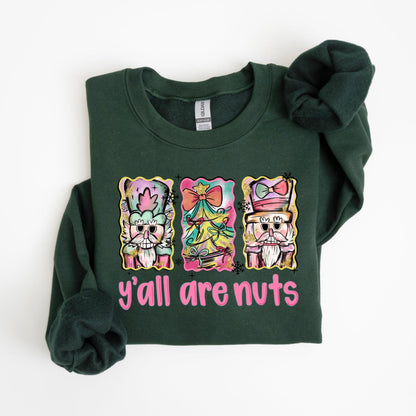 May include: Dark green sweatshirt with a graphic that says "y'all are nuts." The graphic features three colorful images of nutcrackers and a Christmas tree. The sweatshirt is made of a soft material.