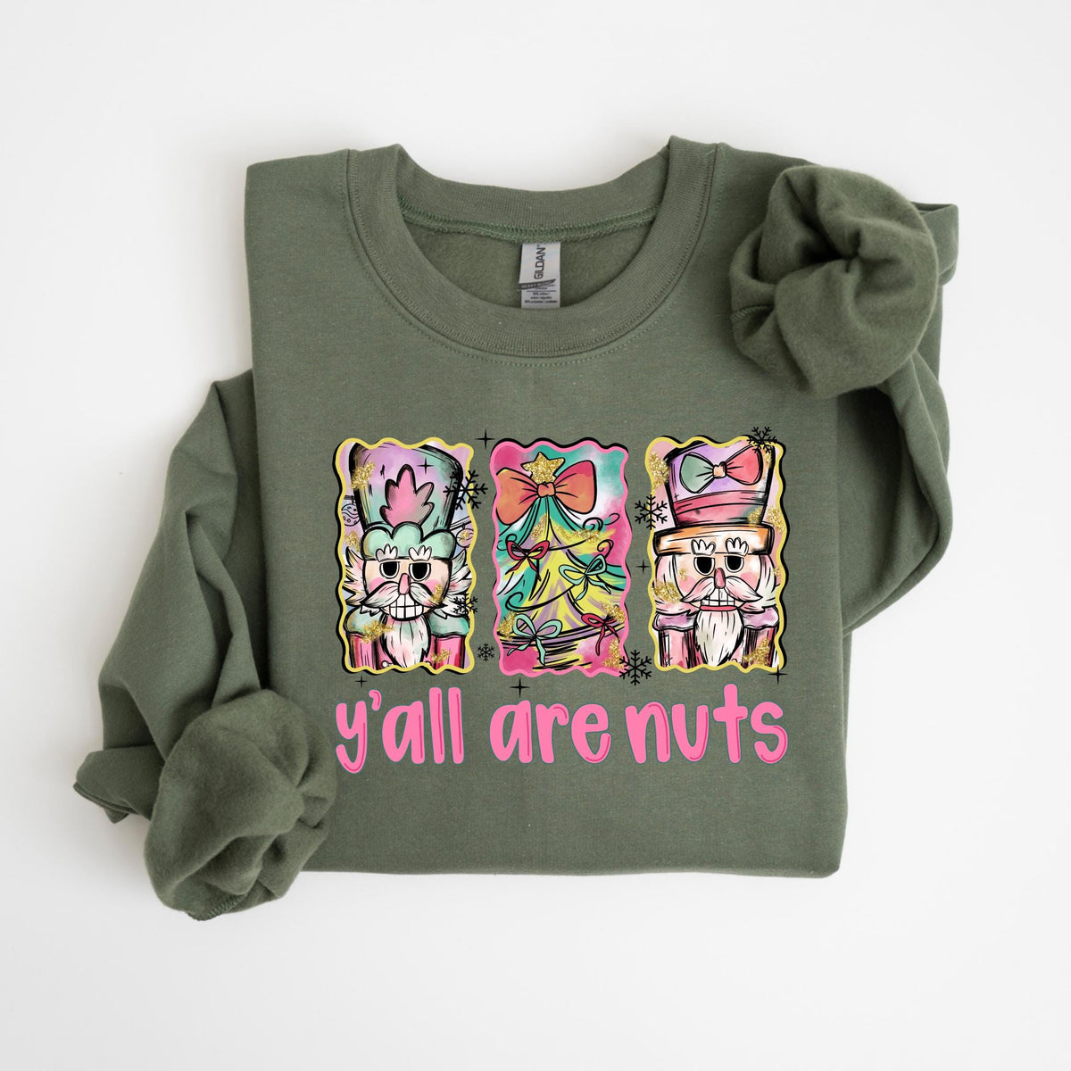 May include: Olive green sweatshirt with a colorful graphic of three nutcrackers and a Christmas tree. The text "y'all are nuts" is in pink. The sweatshirt is made of a soft material.