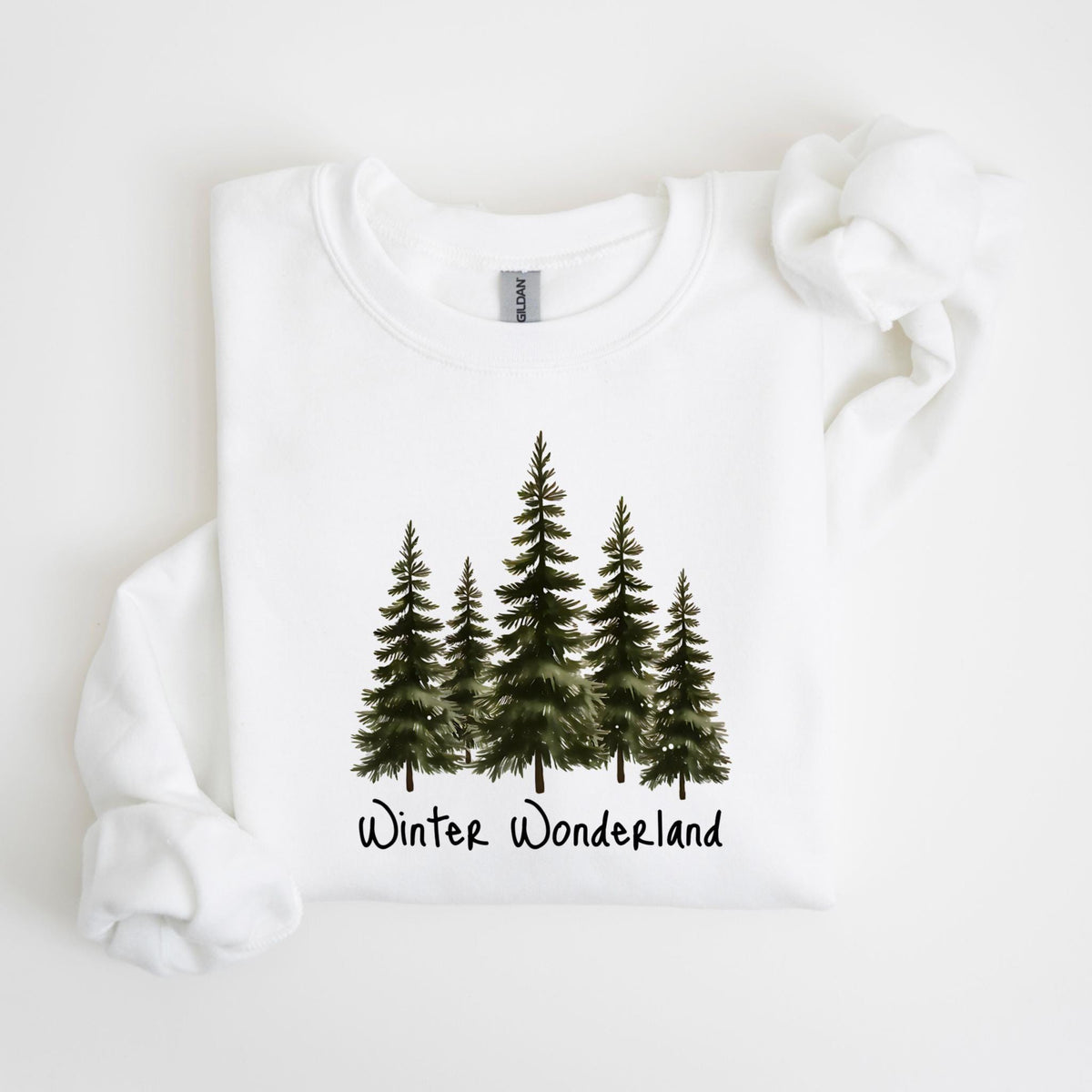 May include: White sweatshirt featuring a watercolor design of five evergreen trees in varying sizes. Below the trees, the words "Winter Wonderland" are written in a handwritten style font. The sweatshirt has a crew neck and long sleeves.