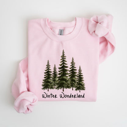 May include: A light pink sweatshirt featuring a watercolor illustration of five evergreen trees. The words "Winter Wonderland" are printed in a script font below the trees. The sweatshirt has a crew neck and long sleeves.