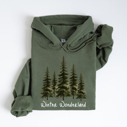 May include: An olive green hoodie featuring a watercolor illustration of evergreen trees. The phrase "Winter Wonderland" is printed in white script at the bottom of the design. The hoodie has a drawstring hood and long sleeves.