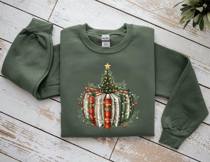May include: Olive green sweatshirt featuring a Christmas tree design atop a stack of books. The tree is adorned with a gold star and string lights. The books have red and green spines. The sleeves are long and have a gathered detail at the wrist.