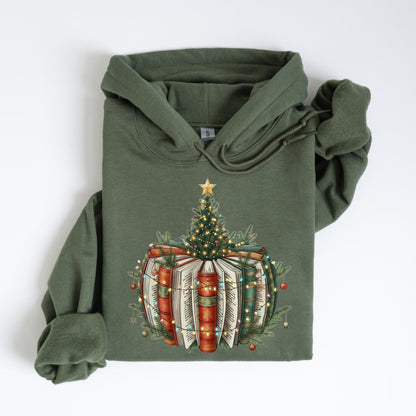 May include: Olive green hoodie featuring a Christmas tree design atop a stack of books. The books are red, green, and white, adorned with fairy lights and a star on top of the tree. The hoodie has a drawstring hood and long sleeves.