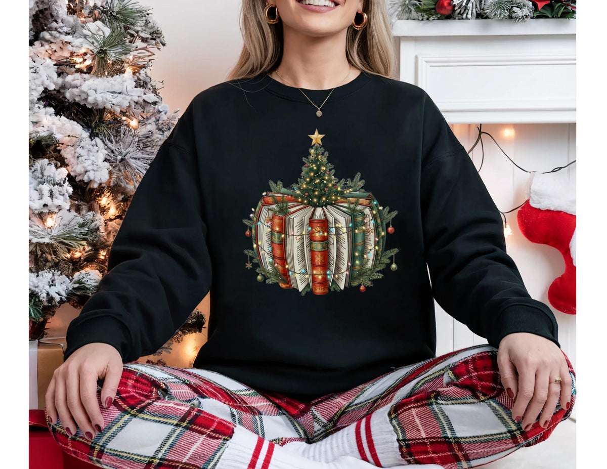 May include: Black sweatshirt featuring a Christmas tree design atop a stack of books. The design includes a star, fairy lights, and festive greenery. The wearer is also wearing red and white plaid pajama pants.