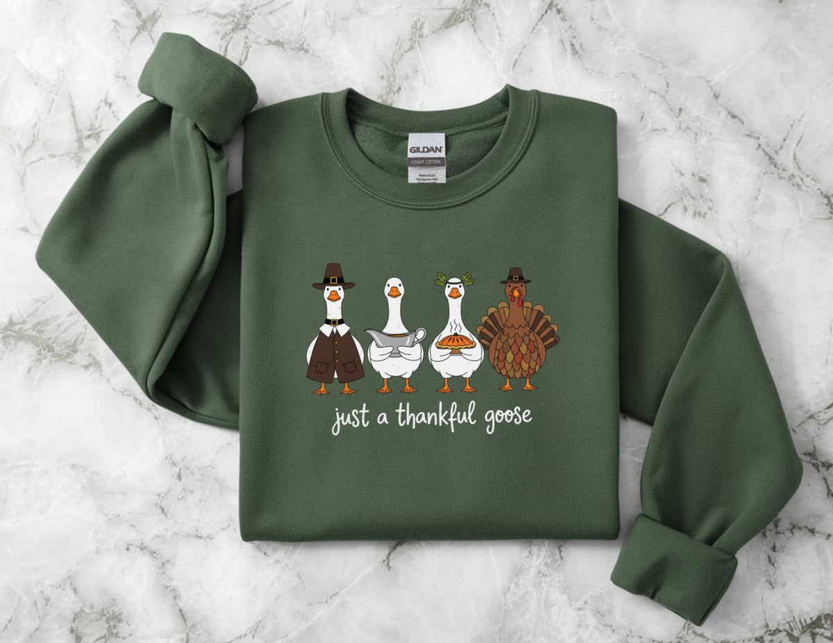 May include: A dark green sweatshirt featuring a graphic of four cartoon geese and a turkey, each dressed in Thanksgiving attire. The text "just a thankful goose" is printed below the characters. The sweatshirt has long sleeves and a crew neck.