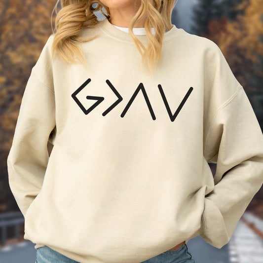 May include: A beige sweatshirt with the black text "G>AV" printed across the chest. The sweatshirt has long sleeves and a crew neck. The background is blurred, with autumn colors visible.