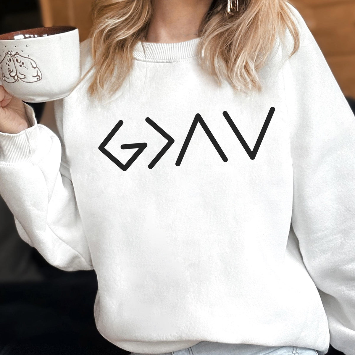 May include: A white sweatshirt with the word "GAV" in black block letters. The sweatshirt is a crew neck style. A person is holding a white mug with a brown interior and a drawing of two dogs.