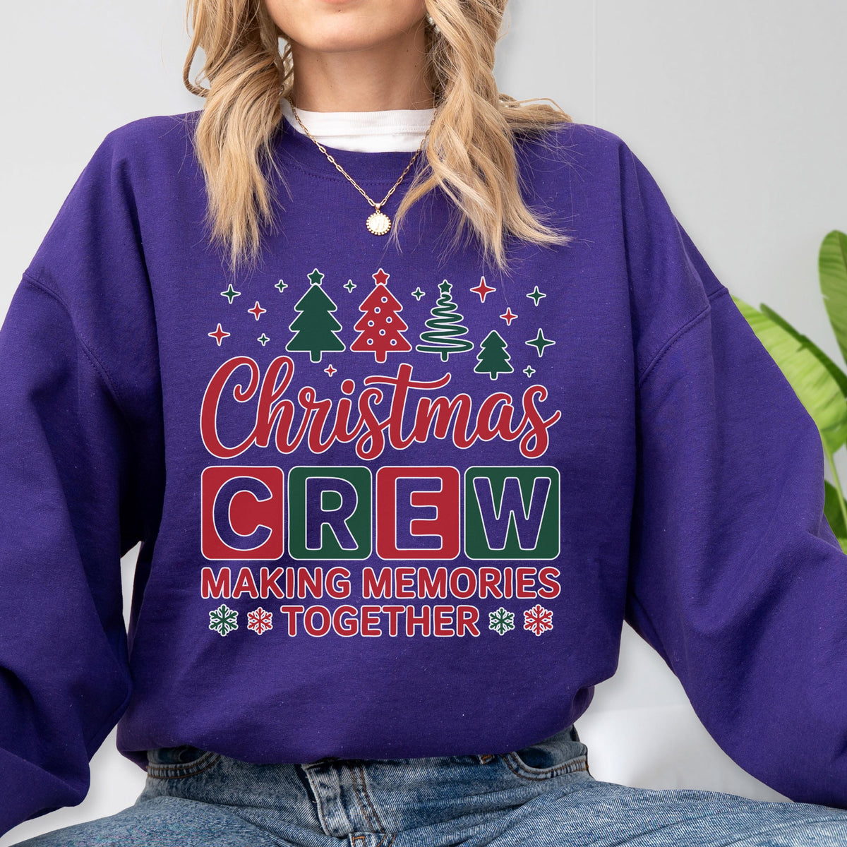 May include: A purple long-sleeve sweatshirt featuring a graphic print with the text "Christmas CREW MAKING MEMORIES TOGETHER" in red, white, and green. The design includes illustrations of various Christmas trees and small snowflake icons.