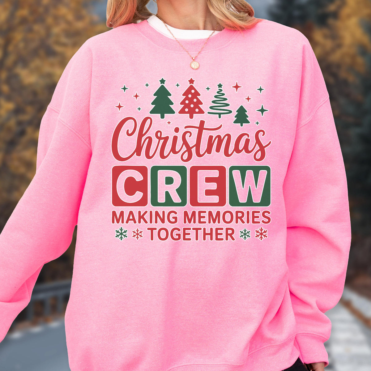 May include: A bright pink long-sleeve sweatshirt featuring a graphic print with the text "Christmas CREW MAKING MEMORIES TOGETHER". The design includes red and green stylized Christmas trees, snowflakes, and stars arranged above and below the text.