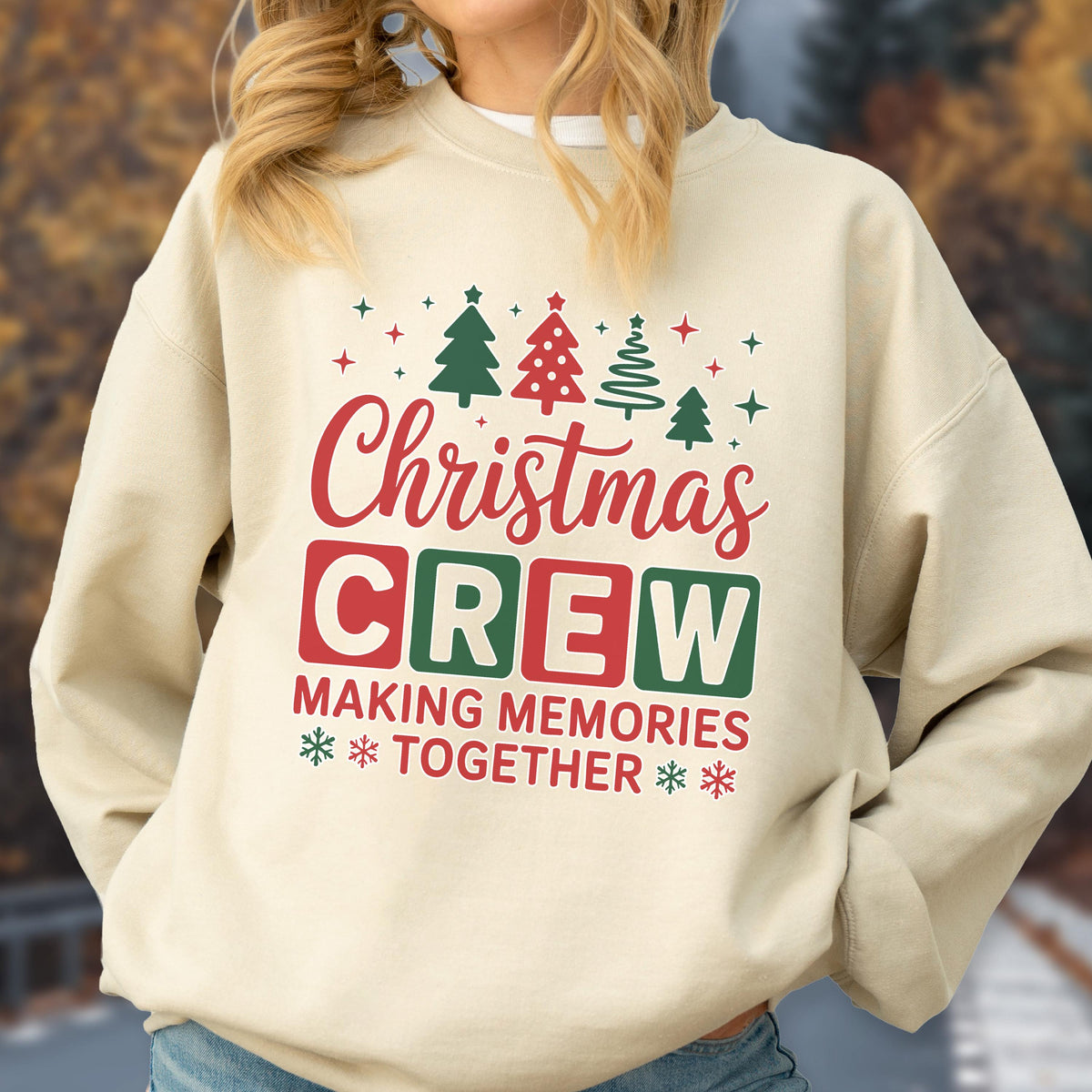 May include: A beige crewneck sweatshirt featuring a graphic print with red and green Christmas trees, stars, and snowflakes. The text reads "Christmas CREW" in red and green block letters, followed by "MAKING MEMORIES TOGETHER" in red text.