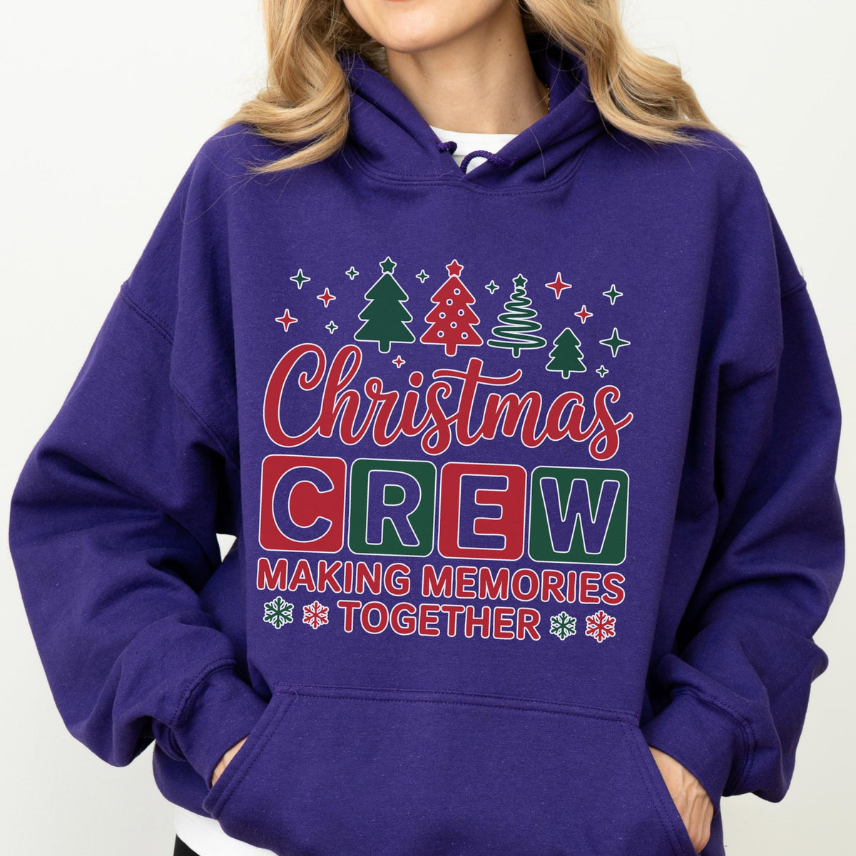 May include: A purple hooded sweatshirt featuring a graphic print with the text Christmas CREW MAKING MEMORIES TOGETHER. The design includes red and green block letters, stylized Christmas trees, and small snowflake icons in red and white.